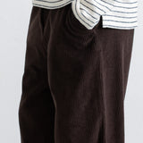 Close-up of a person wearing dark brown corduroy trousers and a white long-sleeve shirt with thin black horizontal stripes, cropped from the chest down against a plain light background.