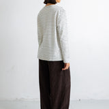 A model shown from the back wearing a cream-colored long-sleeve shirt with thin dark horizontal stripes and dark brown wide-leg trousers, standing against a plain white wall.