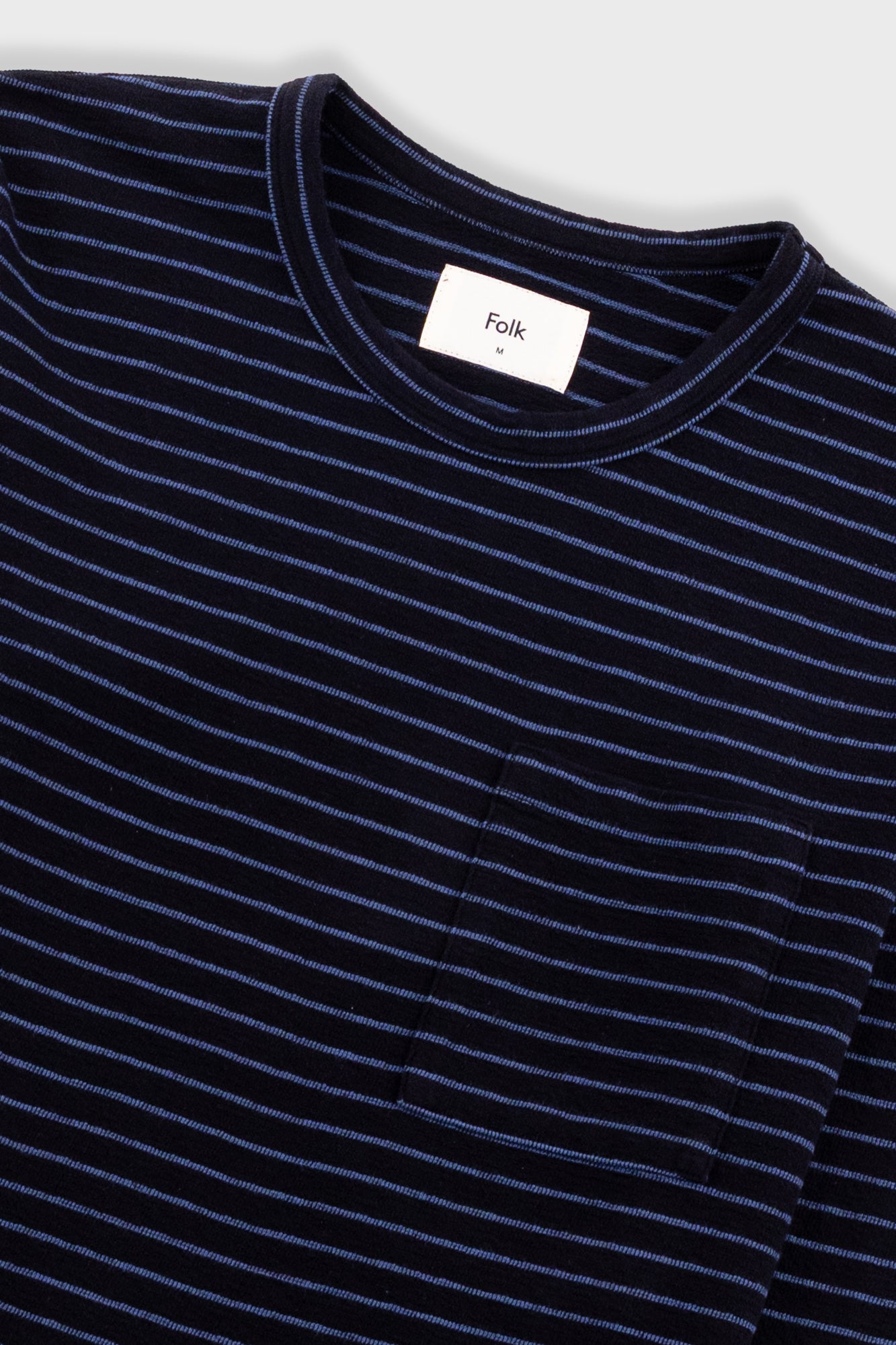 Close-up of a dark navy blue striped crewneck t-shirt with a white neck label reading 'Folk'.