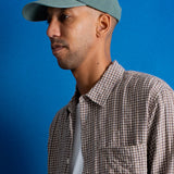 man wearing a plaid shirt and pale green cap with embroidered design on the front
