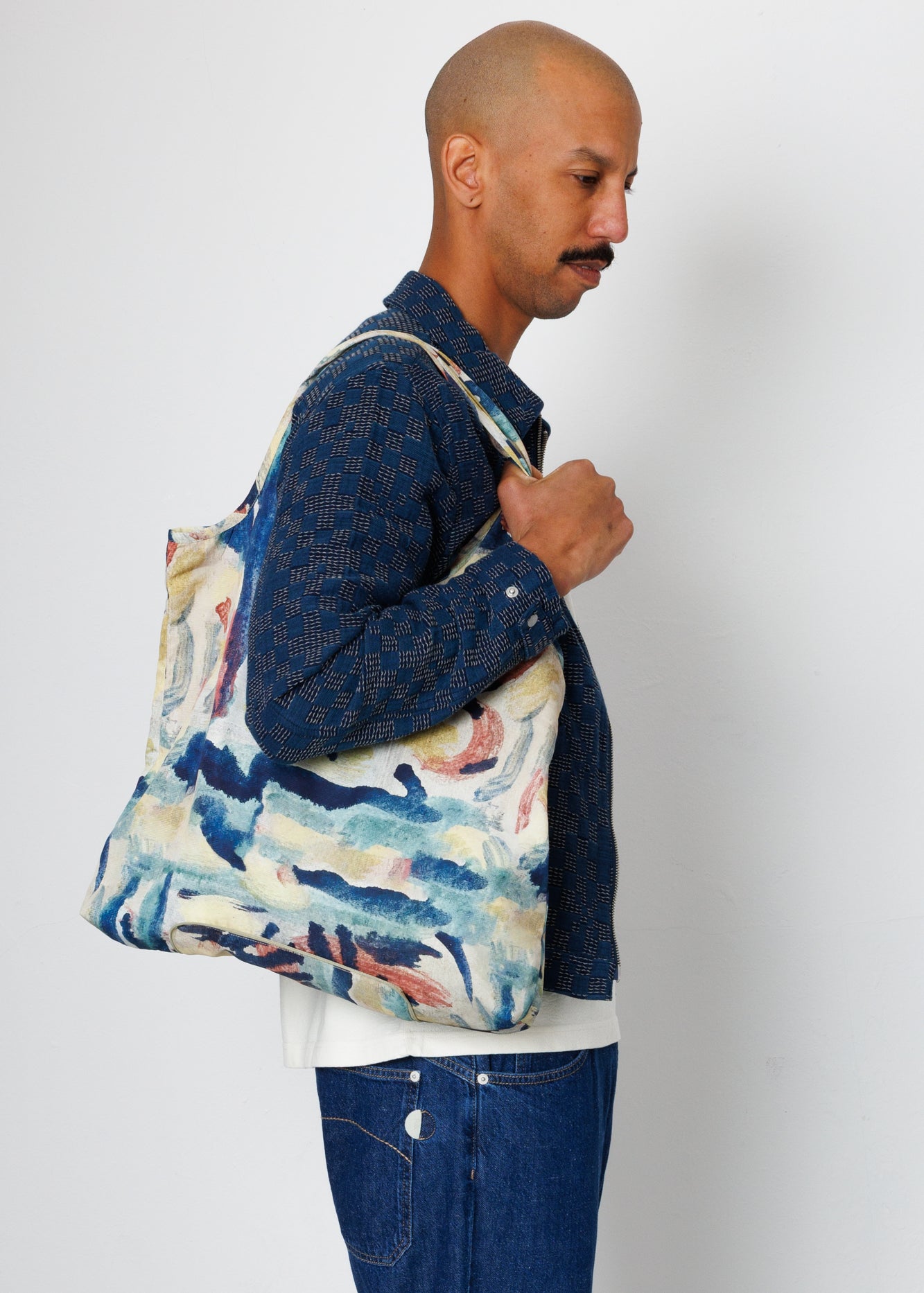 Side view of a male model carrying an impasto Folk tote bag.