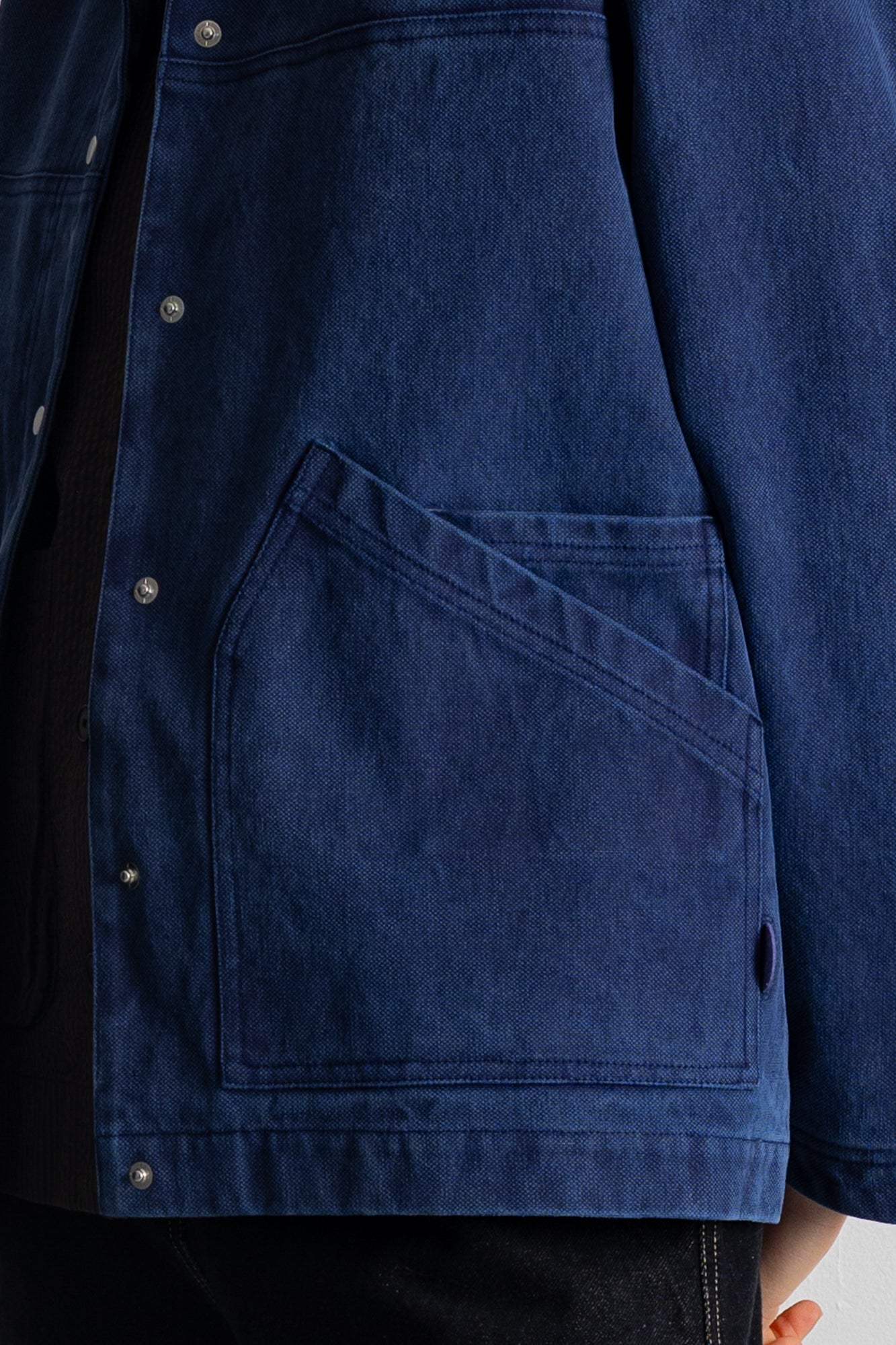 Close-up of a dark blue denim jacket with a large diagonal welt pocket and silver metal snap buttons, worn over a black shirt.
