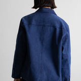 A person shown from the back wearing a dark blue denim jacket and black pants against a plain white wall.