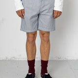Person wearing light gray checkered shorts, white shirt, maroon socks, and black sneakers on a plain background