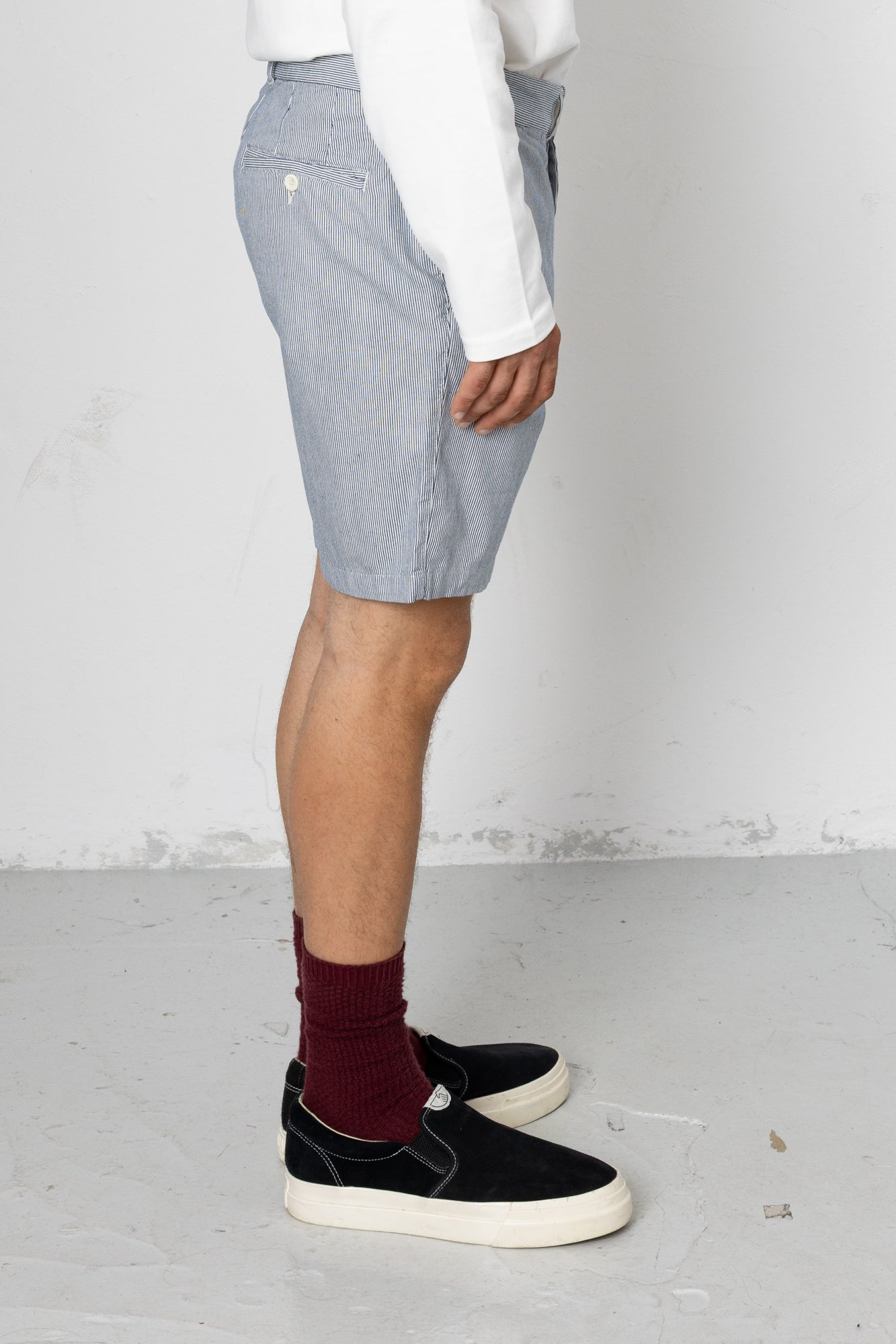 Person wearing light blue shorts, a white shirt, black shoes, and maroon socks on a plain background