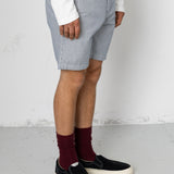 Person wearing light gray shorts, white shirt, maroon socks, and black sneakers on a plain background
