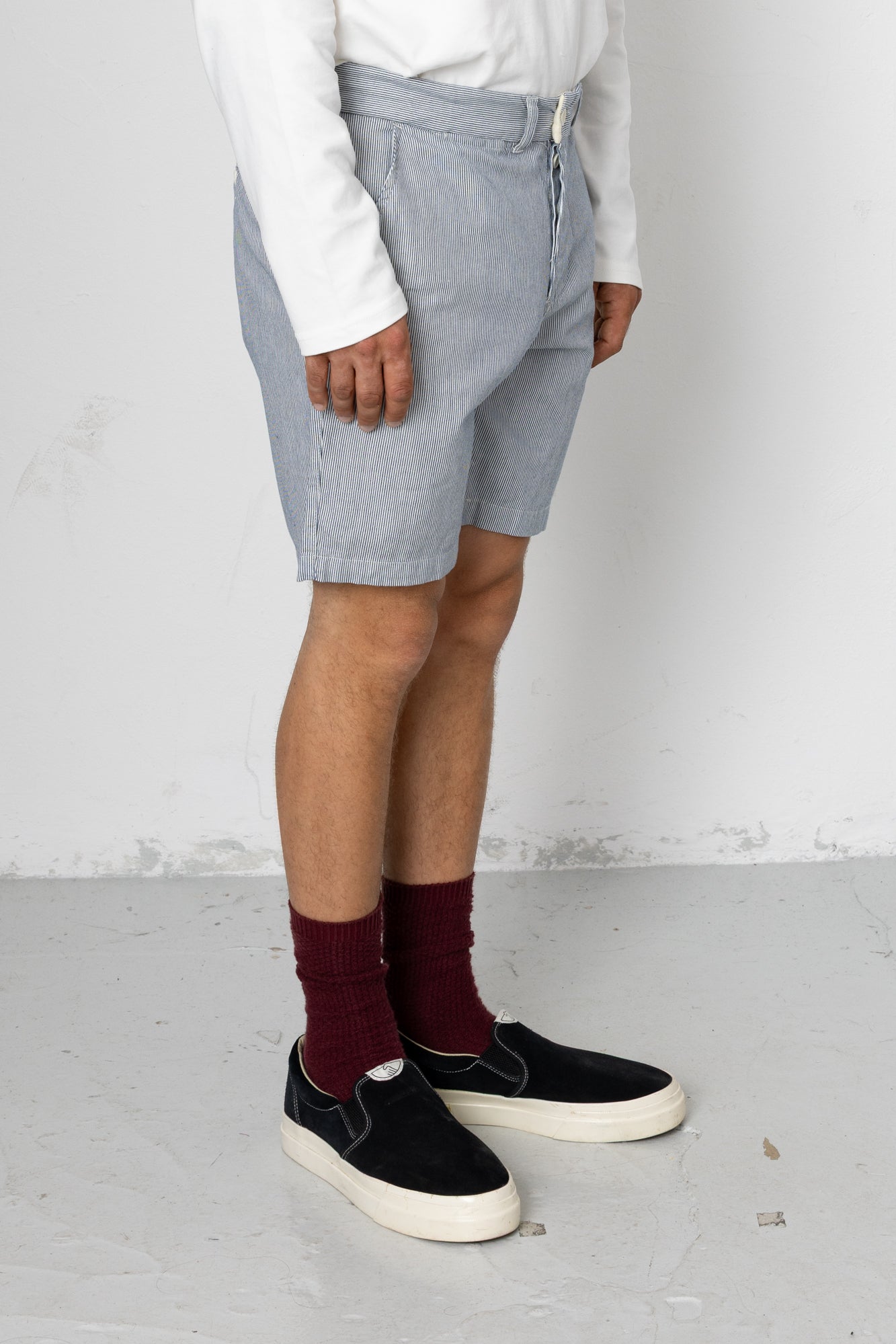 Person wearing light gray shorts, white shirt, maroon socks, and black sneakers on a plain background
