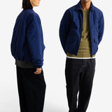 A man and a woman modeling a navy blue lightweight jacket against a clean white studio background. The woman is shown from the back, and the man is shown from the front, both wearing dark pants and sneakers.