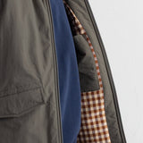 Close-up of a dark gray zip-up jacket worn over a navy blue sweatshirt, showing the interior pocket lined with a brown and beige gingham pattern.