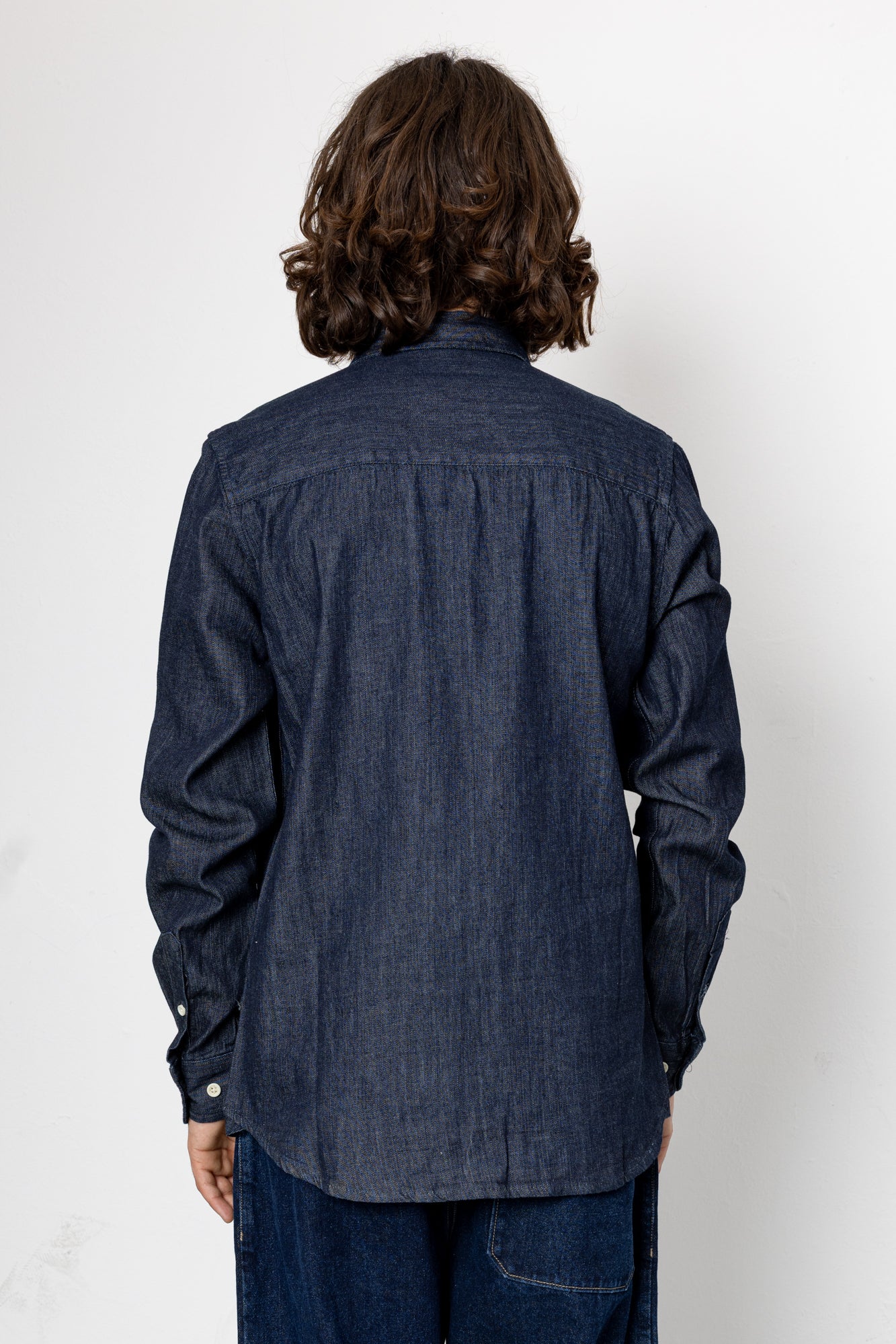 Person wearing a dark denim shirt from behind on a white background