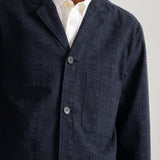 A close-up of a man wearing a dark greytextured jacket over a white collared shirt, cropped from the chin down against a plain light background.