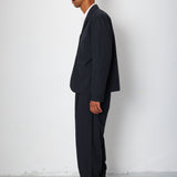 Man wearing a dark suit standing against a white wall