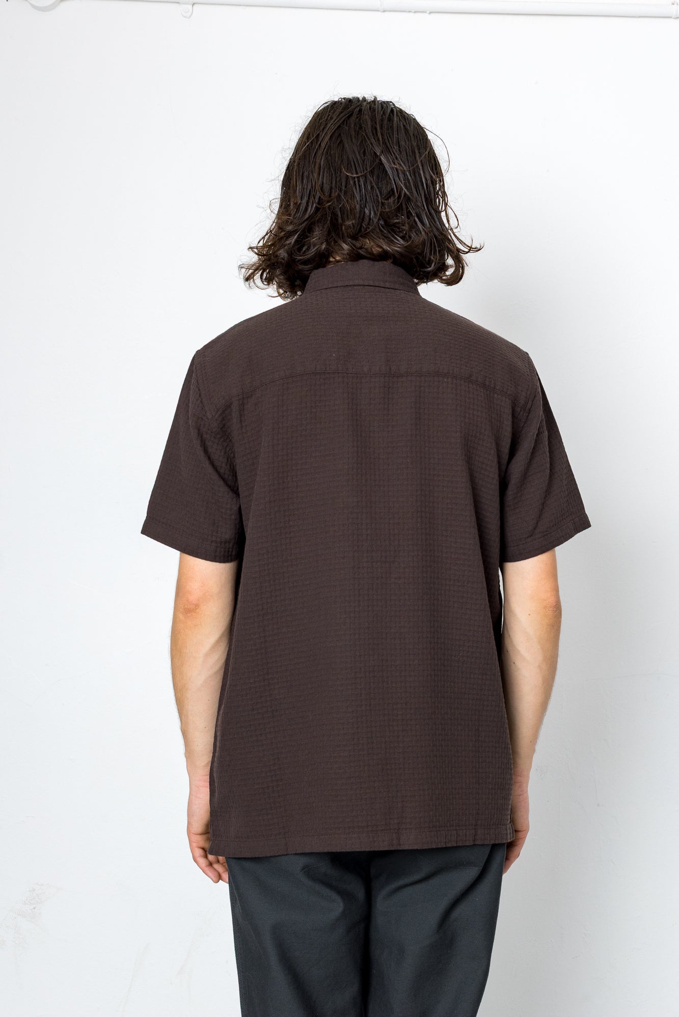 Person wearing a brown short-sleeve shirt against a white background