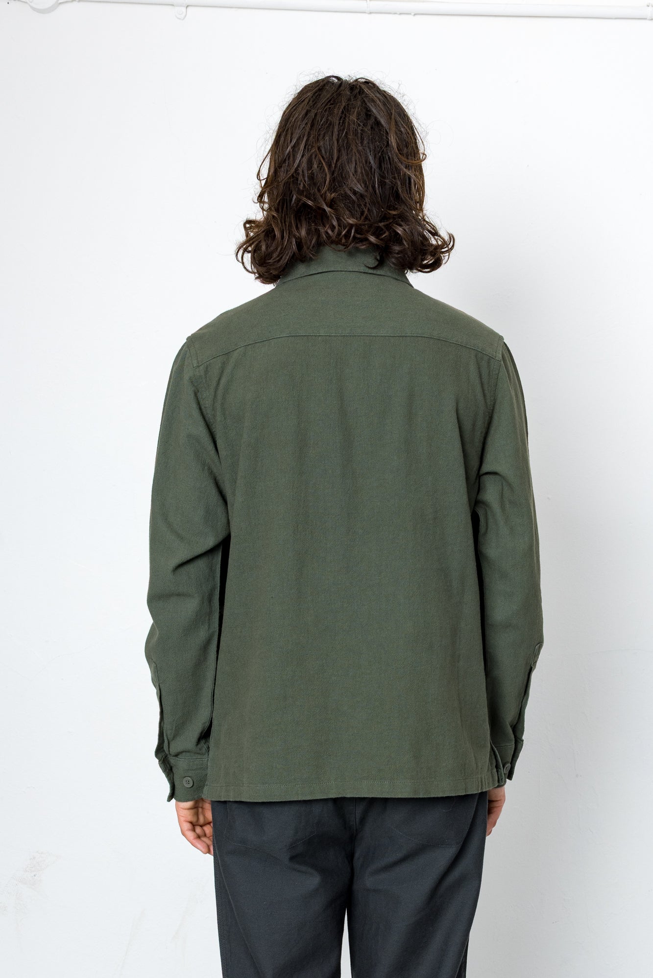 Person wearing a green shirt and dark pants against a white background