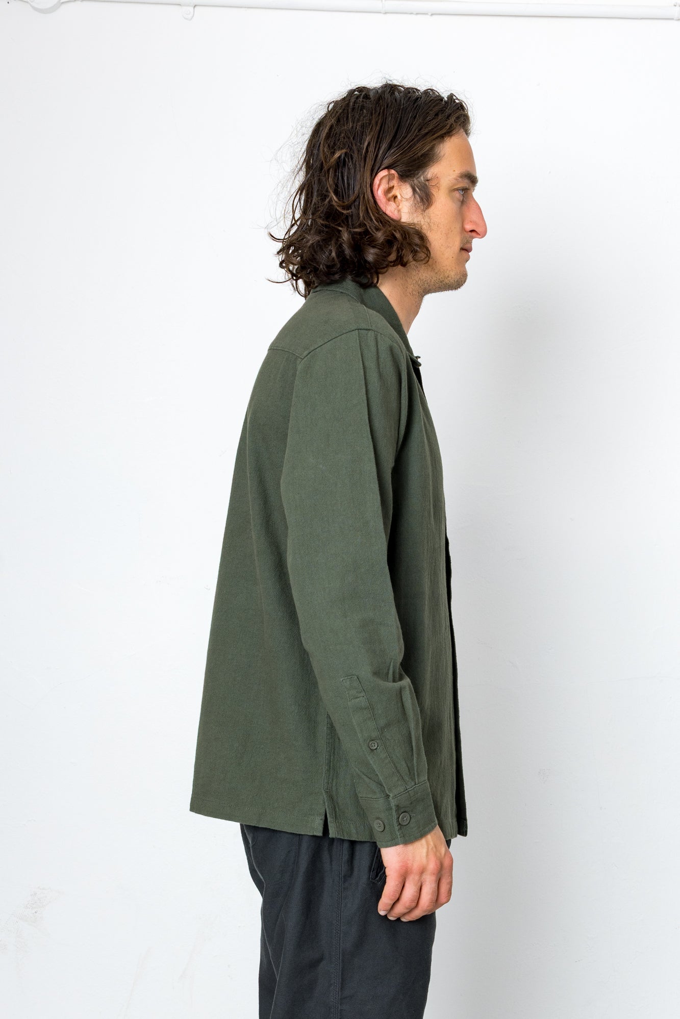 Man wearing a green jacket and dark pants against a white background