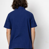 Person wearing a blue textured shirt and black pants against a white background