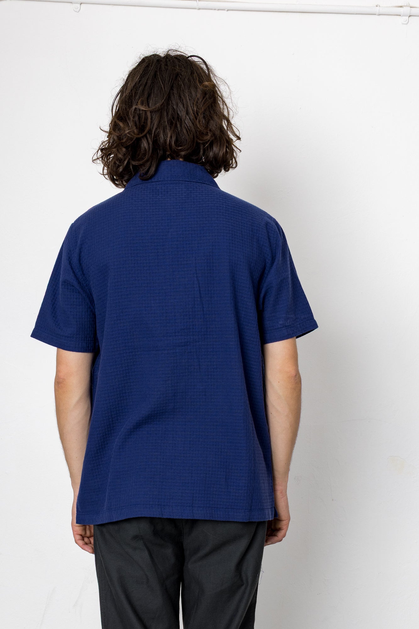 Person wearing a blue textured shirt and black pants against a white background