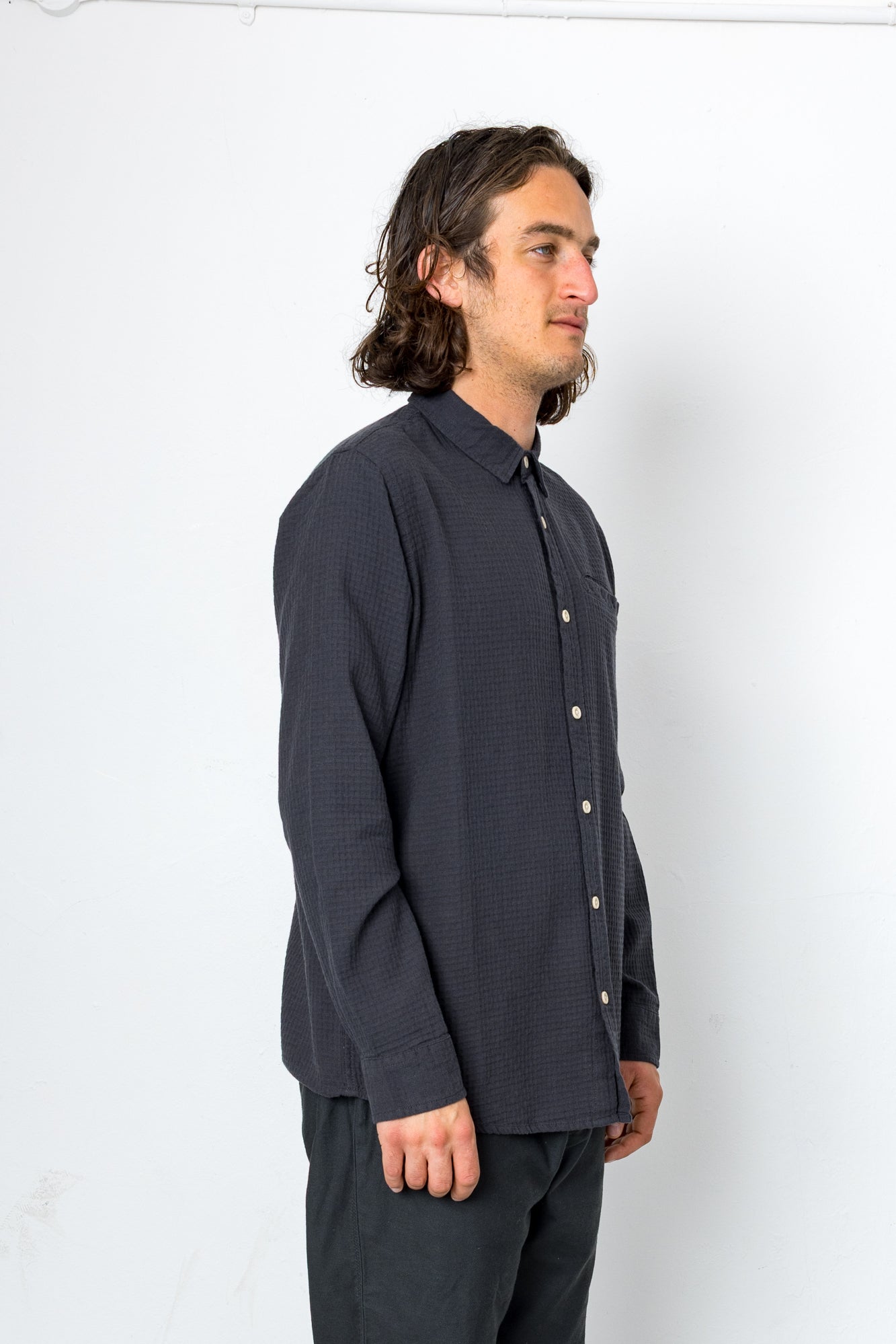 Man wearing a dark gray button-up shirt and pants against a white background