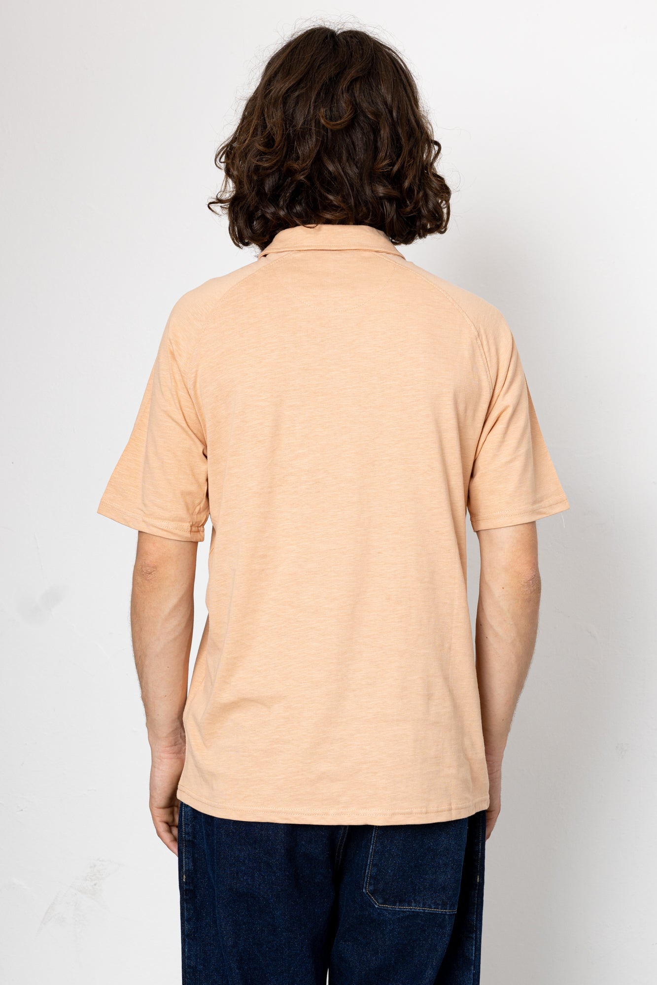 Person wearing a beige polo shirt and dark pants against a white background