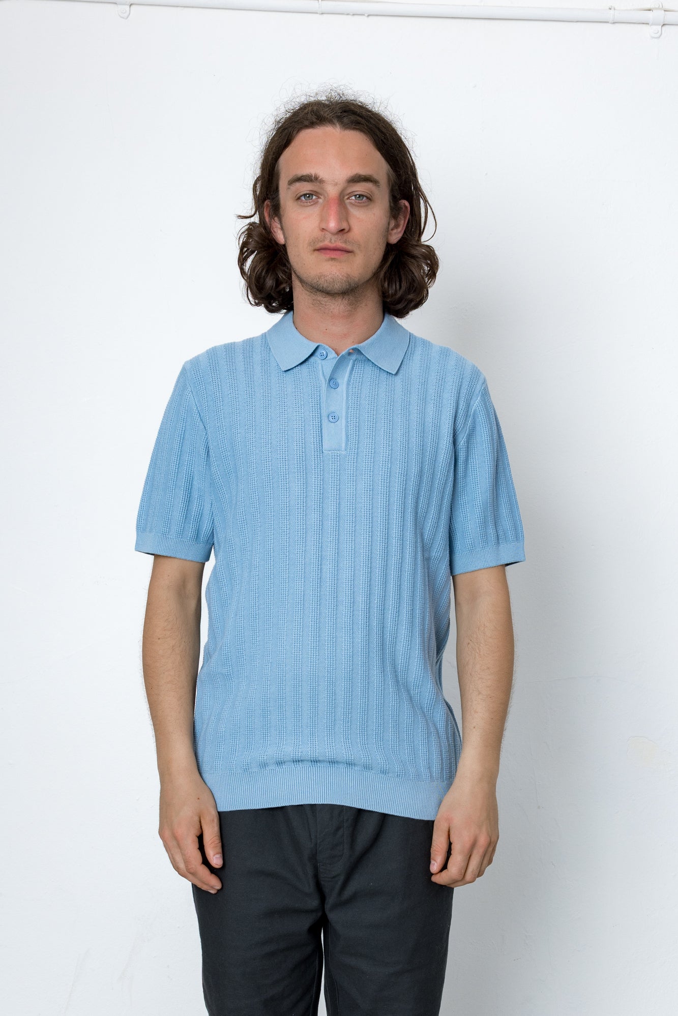 Person wearing a light blue knitted polo shirt against a white background