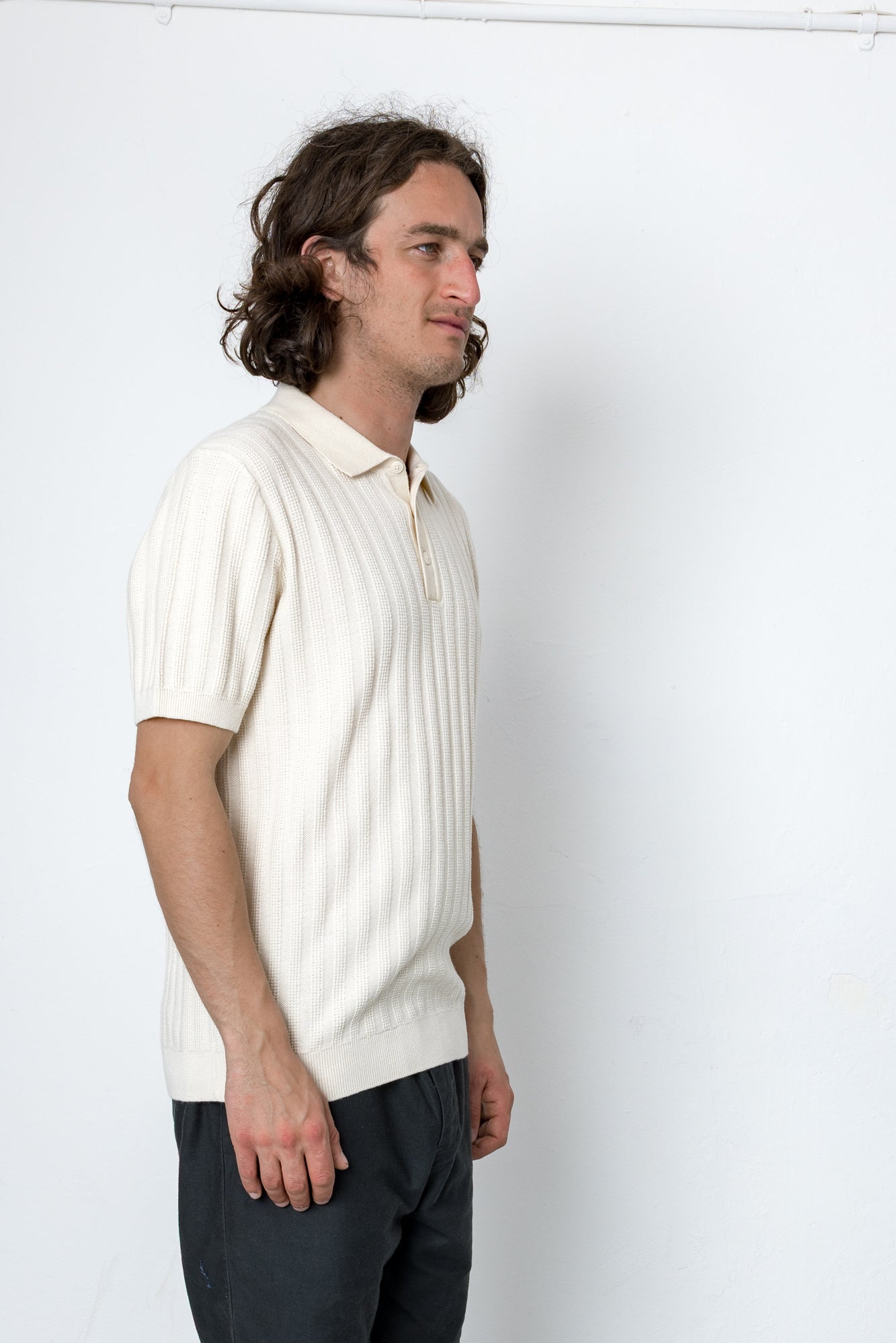 Man wearing a white knit polo shirt and dark pants against a white background