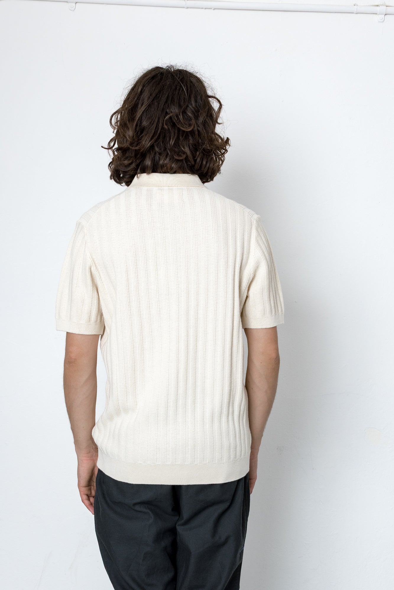Person wearing a white ribbed knit polo shirt against a plain background