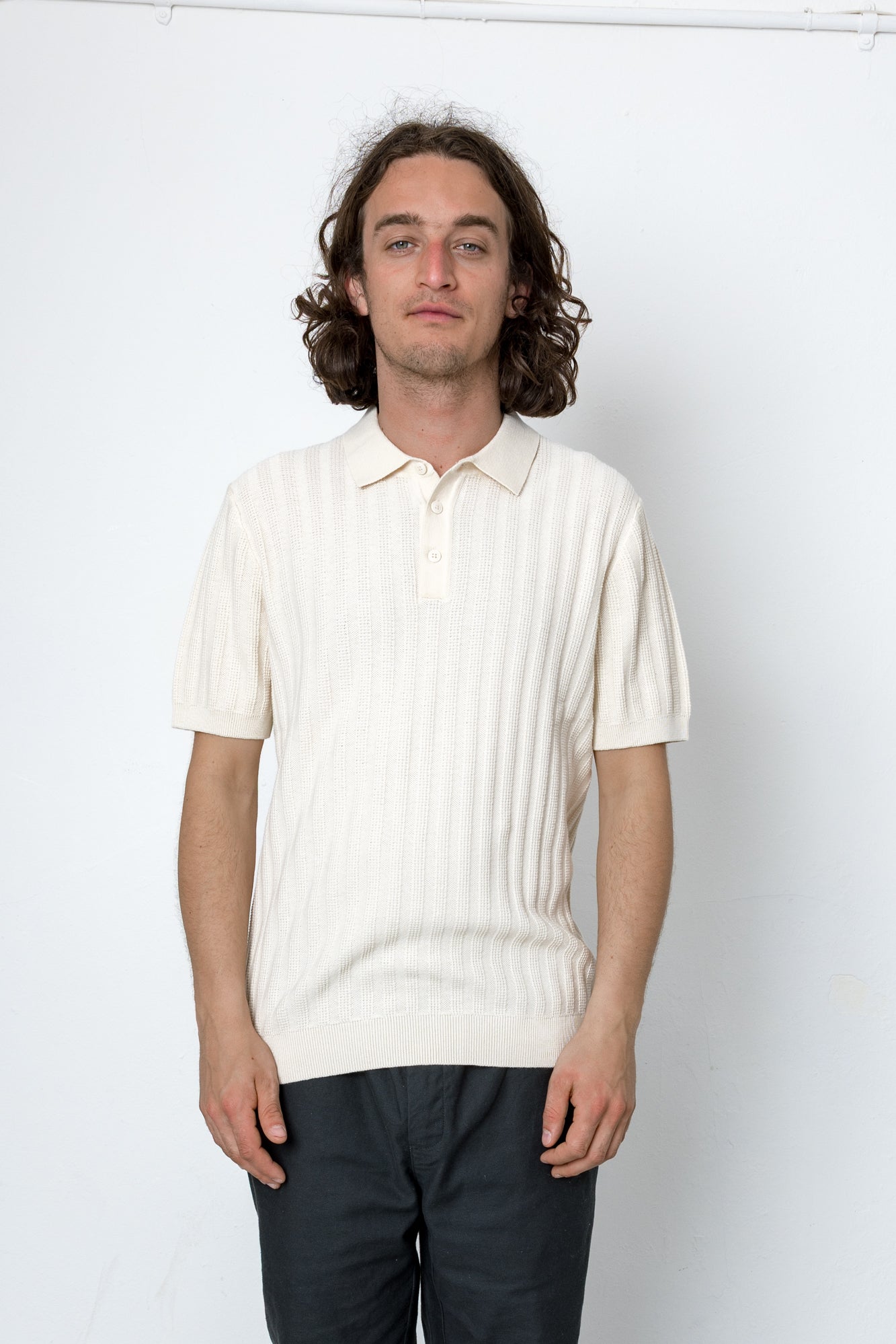 Man wearing a cream-colored knit polo shirt against a white background