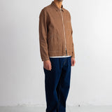 A man wearing a brown corduroy jacket, dark blue jeans, a navy blue beanie, and black shoes, standing against a white studio wall.