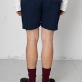 Person wearing navy shorts and maroon socks standing against a white wall.