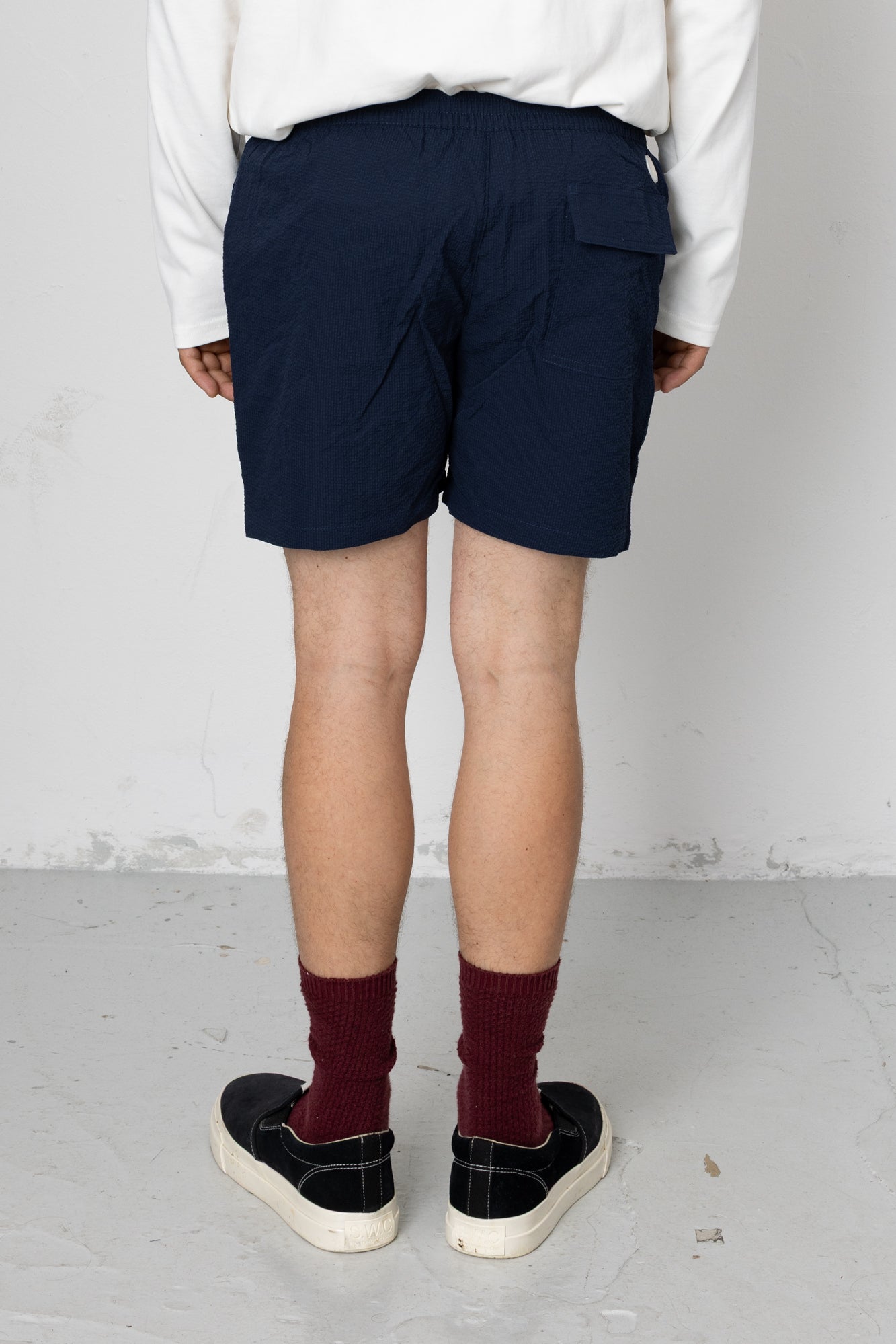 Person wearing navy shorts and maroon socks standing against a white wall.
