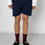 Person wearing navy shorts, white shirt, maroon socks, and black shoes on a plain background