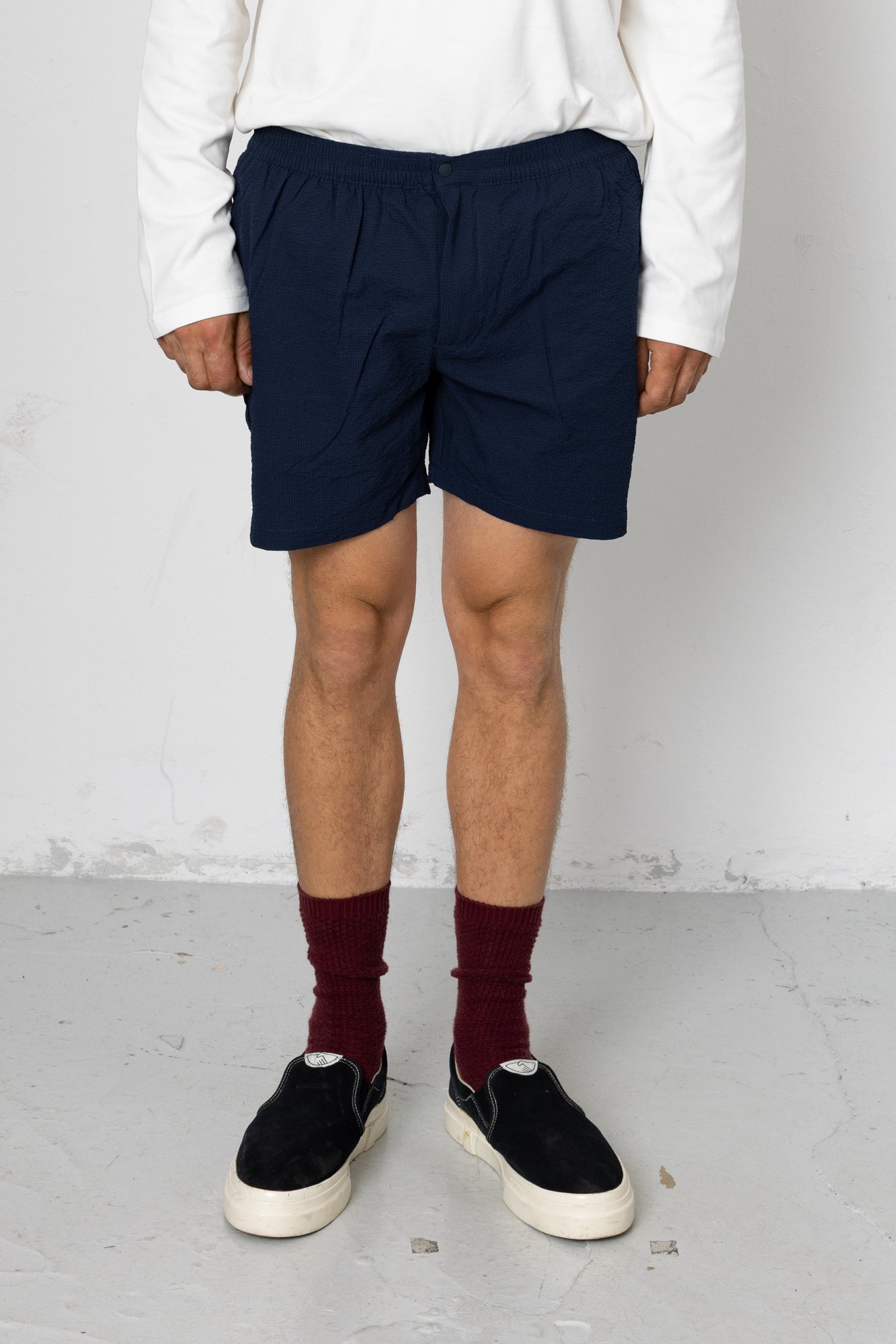 Person wearing navy shorts, white shirt, maroon socks, and black shoes on a plain background