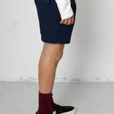 Person wearing navy shorts, white shirt, maroon socks, and black shoes on a light gray floor.