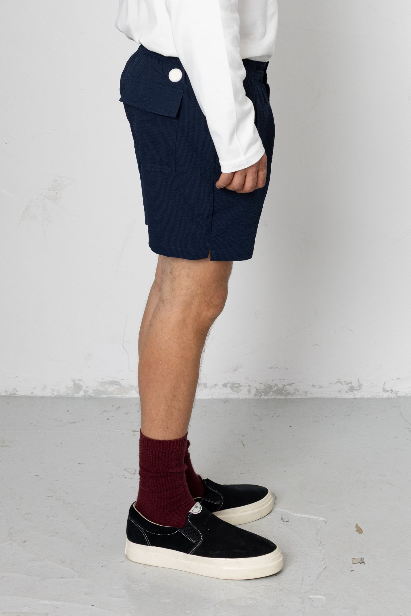 Person wearing navy shorts, white shirt, maroon socks, and black shoes on a light gray floor.