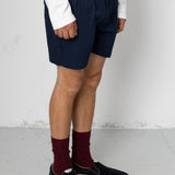 Person wearing navy shorts, white shirt, maroon socks, and black shoes on a plain background