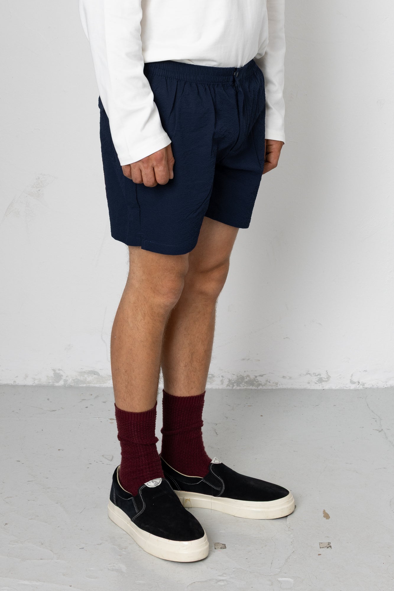 Person wearing navy shorts, white shirt, maroon socks, and black shoes on a plain background