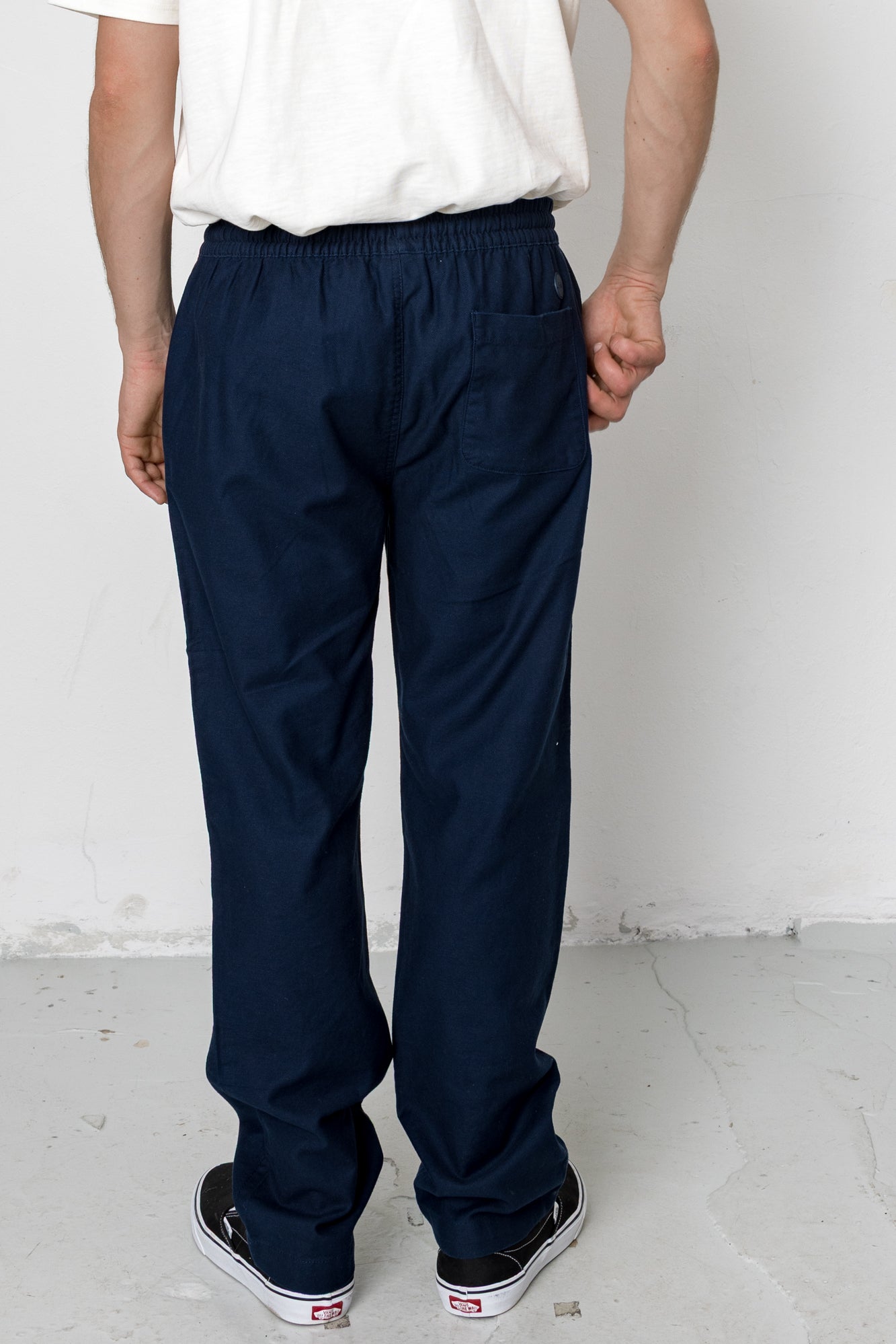Person wearing navy pants and a white shirt against a plain background
