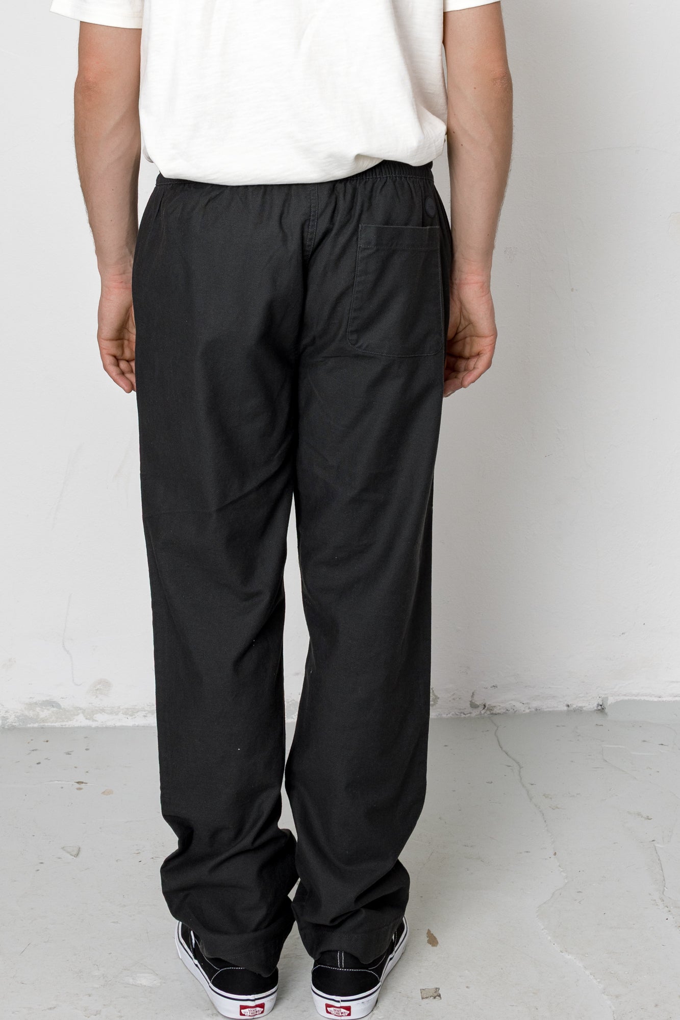 Person wearing black pants and a white shirt against a plain background