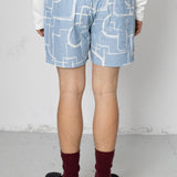 Person wearing light blue shorts with white geometric patterns on a plain background