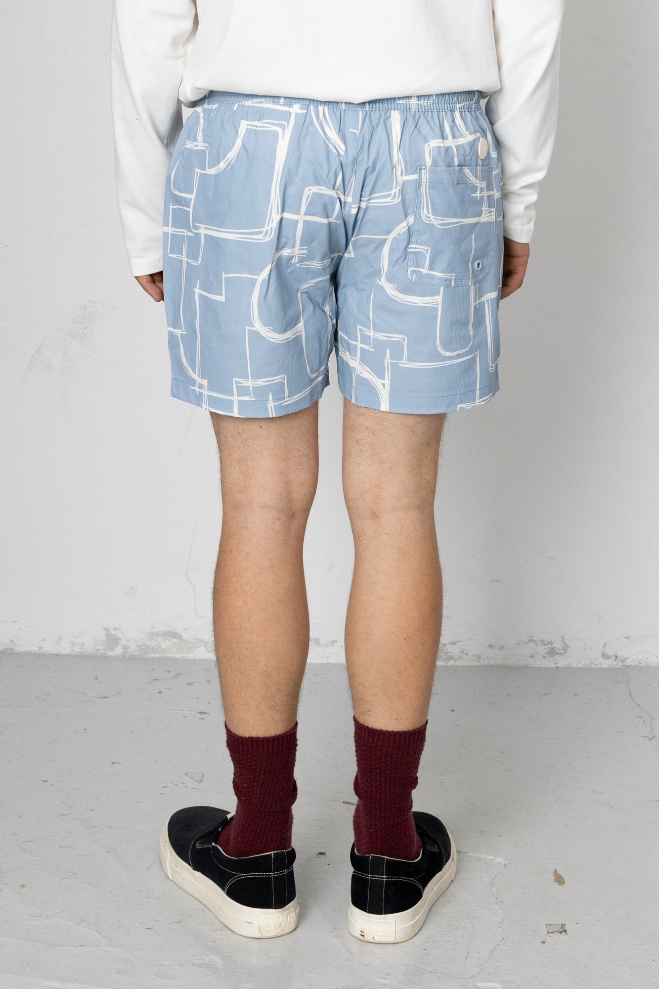 Person wearing light blue shorts with white geometric patterns on a plain background