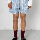 Person wearing blue shorts with white geometric pattern on a plain background
