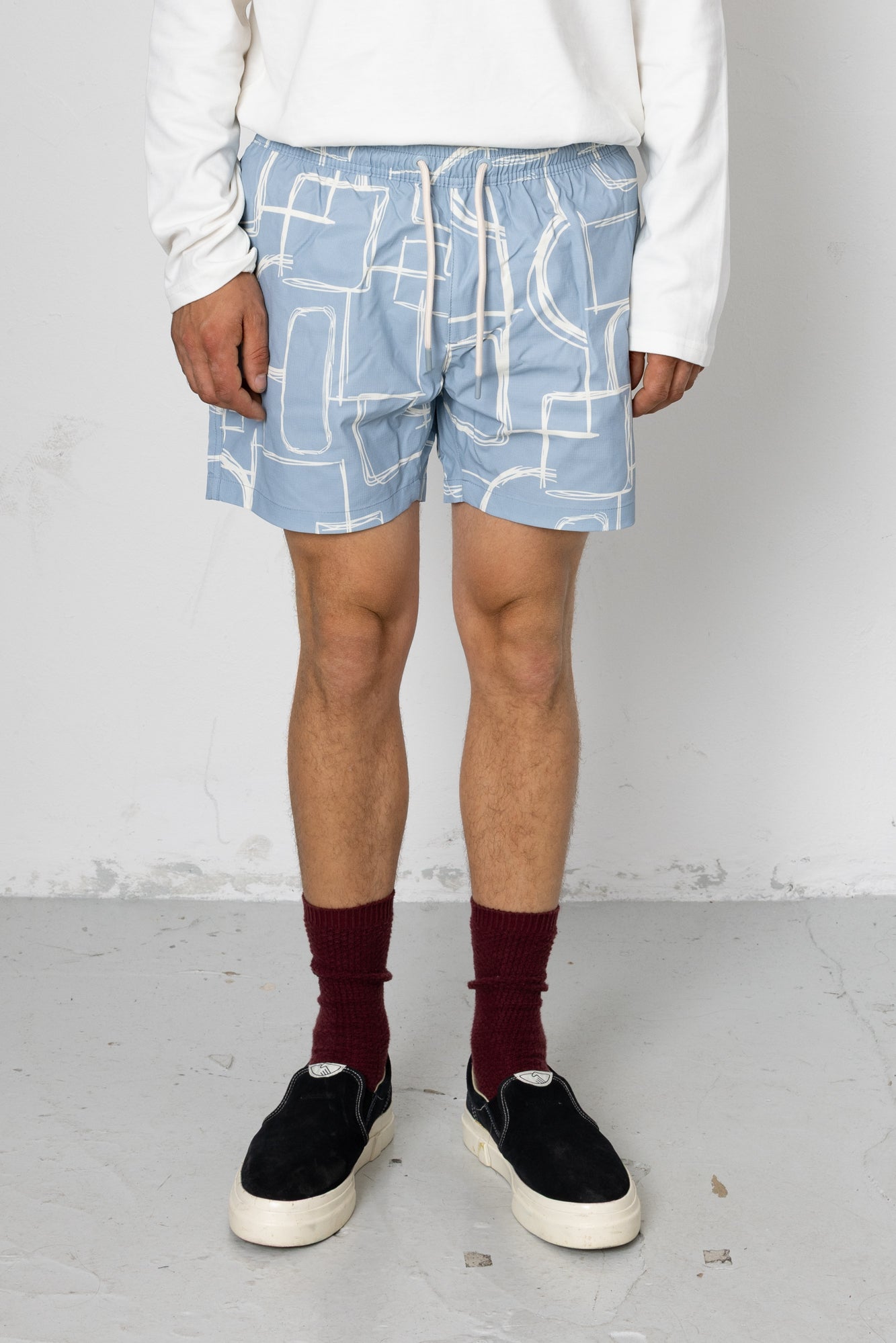 Person wearing blue shorts with white geometric pattern on a plain background