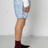Person wearing blue shorts with white geometric pattern on a plain background
