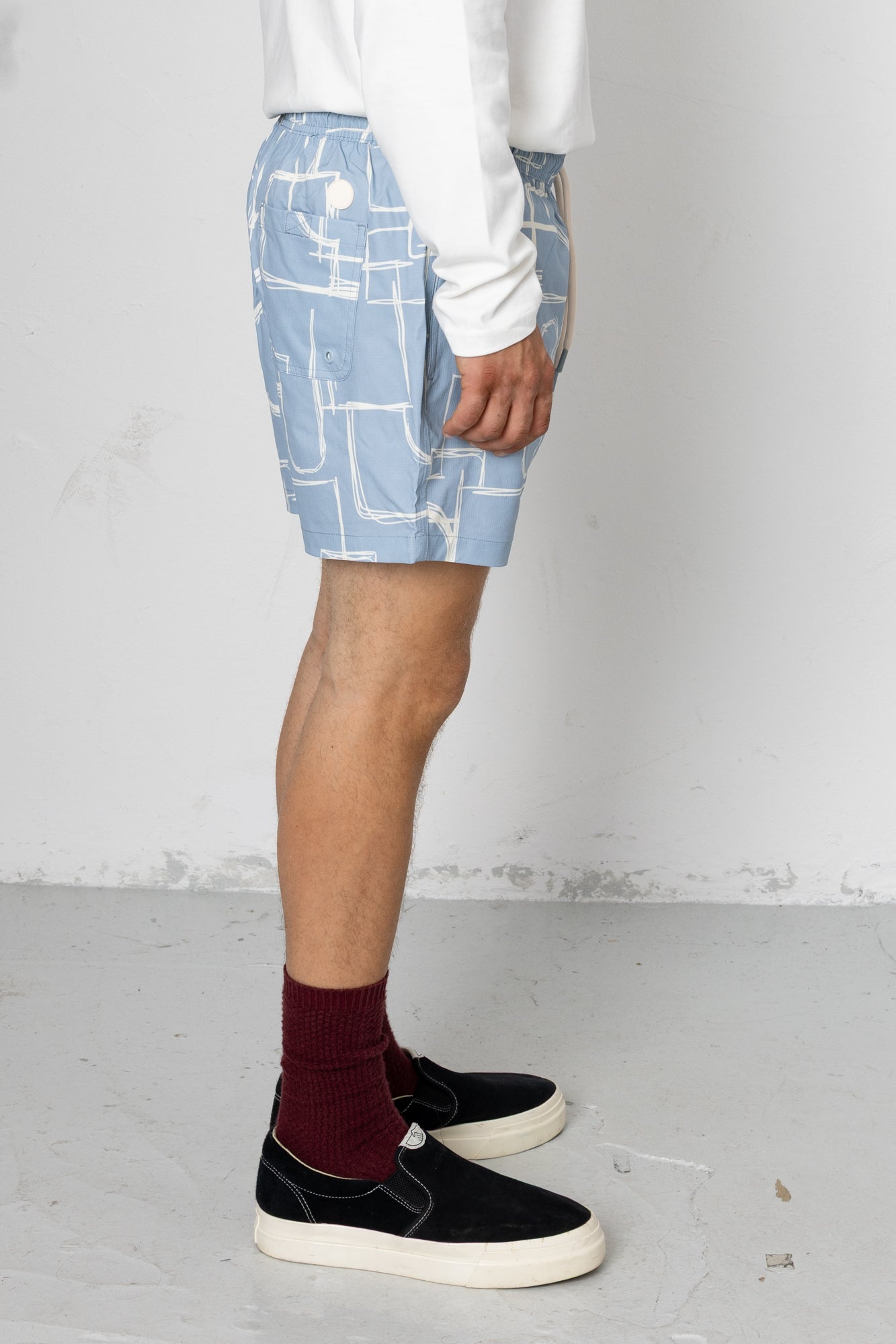 Person wearing blue shorts with white geometric pattern on a plain background