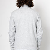 Person wearing a light gray sweater and dark blue pants against a white background