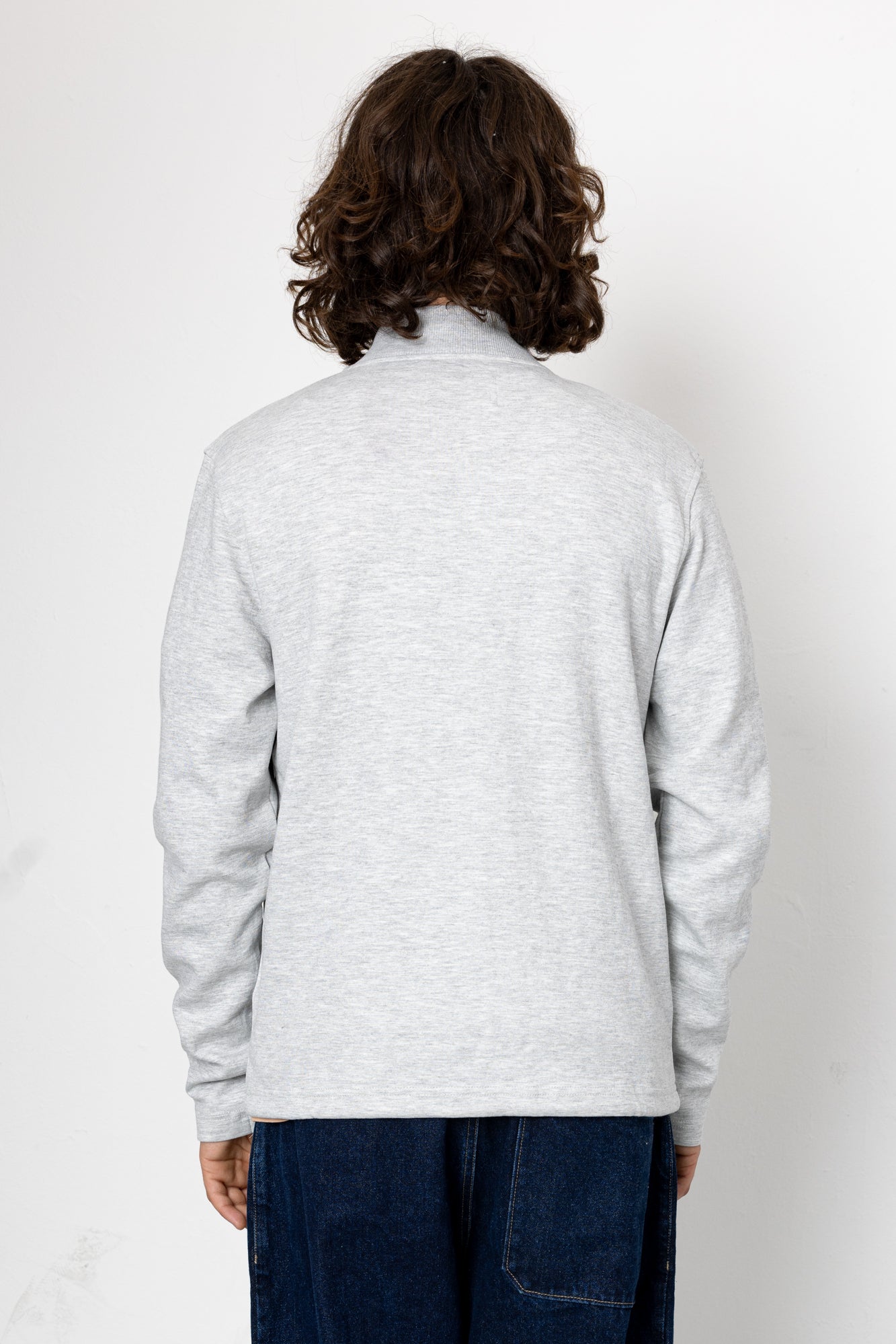 Person wearing a light gray sweater and dark blue pants against a white background