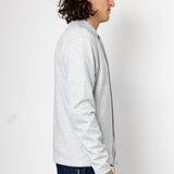 Man wearing a light gray jacket and dark blue jeans on a white background