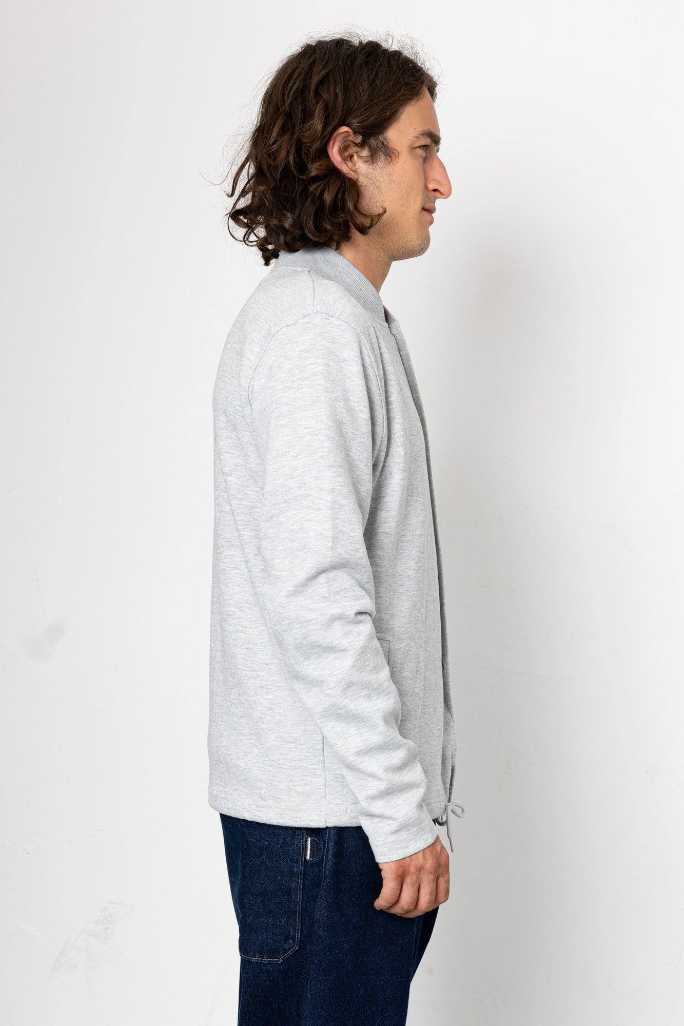 Man wearing a light gray jacket and dark blue jeans on a white background
