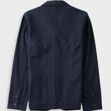 A dark navy blue blazer shown from the back, featuring a clean silhouette with buttoned cuffs and a central seam, photographed against a light gray background.