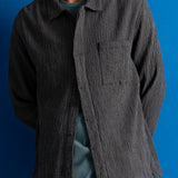 Man wearing textured grey checkered shirt and a dark green cap against a bright blue background